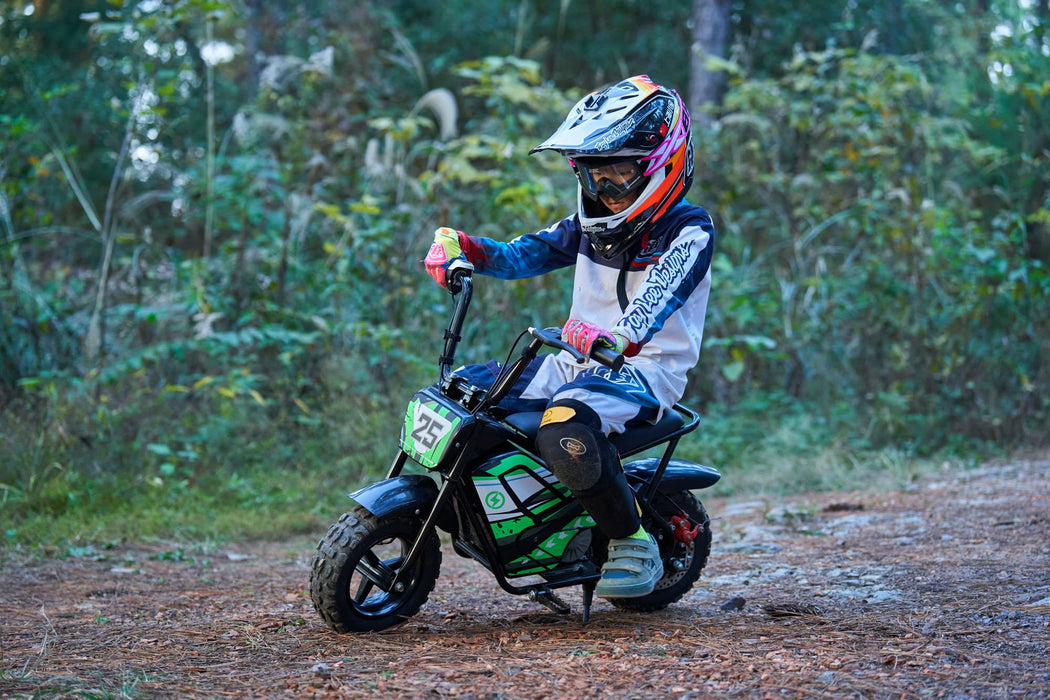 A child in protective gear and helmet rides a MotoTec 24v 250w Electric Mini Bike Black by MotoTec on a rugged forest trail.