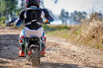 A person in motocross gear rides the MotoTec 24v 250w Electric Mini Bike Black on a forest trail, surrounded by trees.