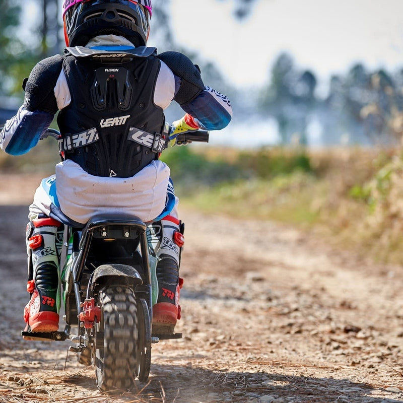 A person in motocross gear rides the MotoTec 24v 250w Electric Mini Bike Black on a forest trail, surrounded by trees.