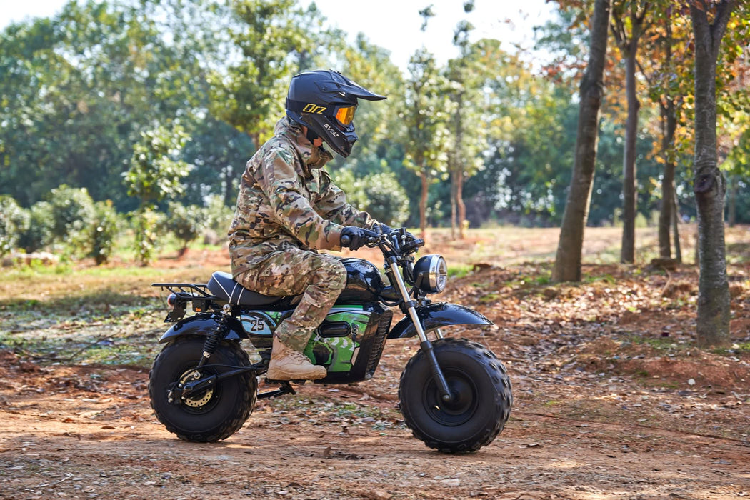 A person in camouflage is riding a MotoTec 60v 1500w Electric Powered Mini Bike Lithium Black with a helmet in a wooded area.