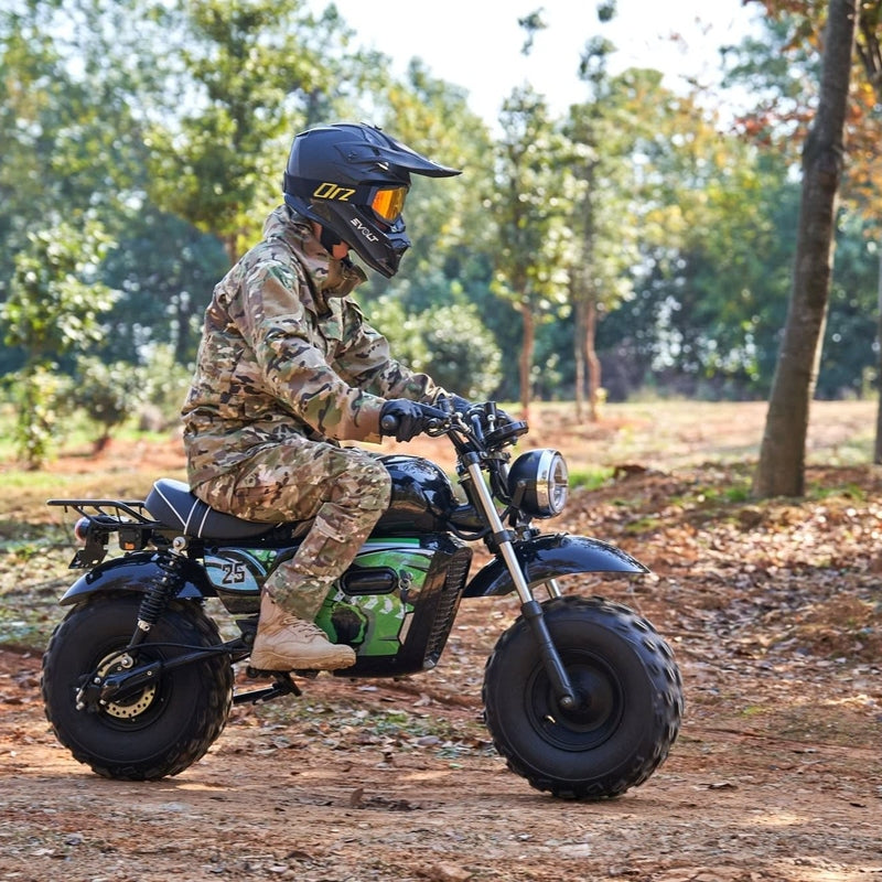 A person in camouflage is riding a MotoTec 60v 1500w Electric Powered Mini Bike Lithium Black with a helmet in a wooded area.