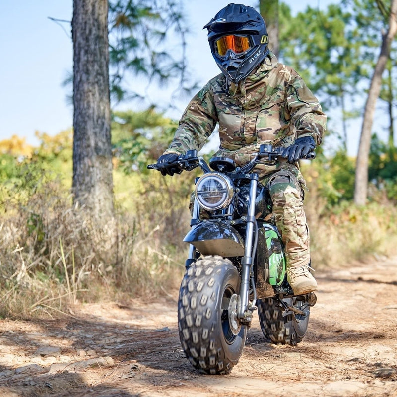 A person in camouflage gear and helmet rides a rugged dirt bike, like the MotoTec 60v 1500w Electric Powered Mini Bike Lithium Black, along a forest trail.