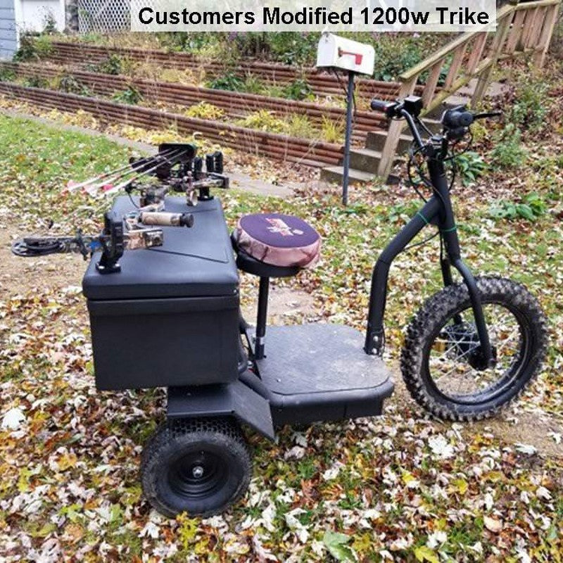 The MotoTec Electric Trike 48v 1200w, an electric-powered trike from the MotoTec brand, featuring chairs and boxes, is shown outdoors on a leafy path.