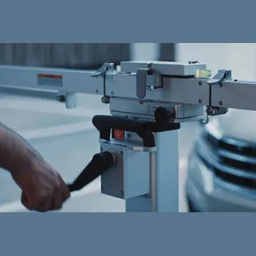 MA600 frame target-arm extension close-up showing the central pivot housing and a technician's hand on the adjustment handle