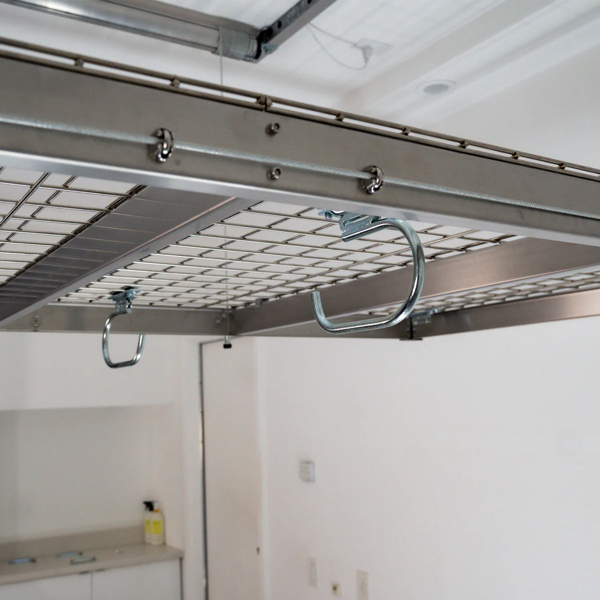 Two zinc-finished hooks installed on the underside wire deck of an overhead garage storage rack