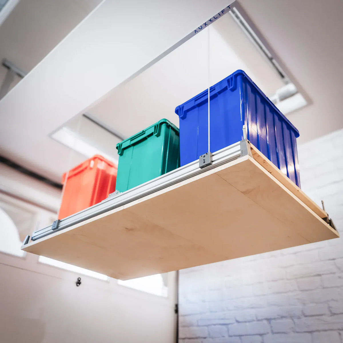 Auxx Lift attic storage platform suspended below a garage ceiling holding three storage totes