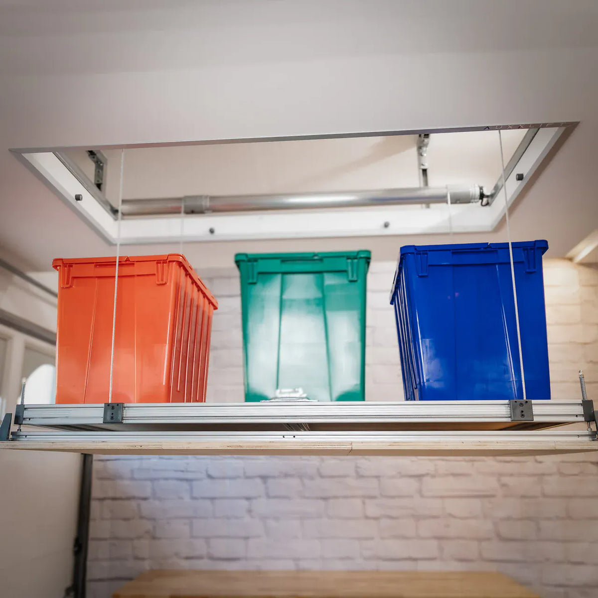 Attic-Lift platform raised below a ceiling cutout, loaded with red, green, and blue storage totes