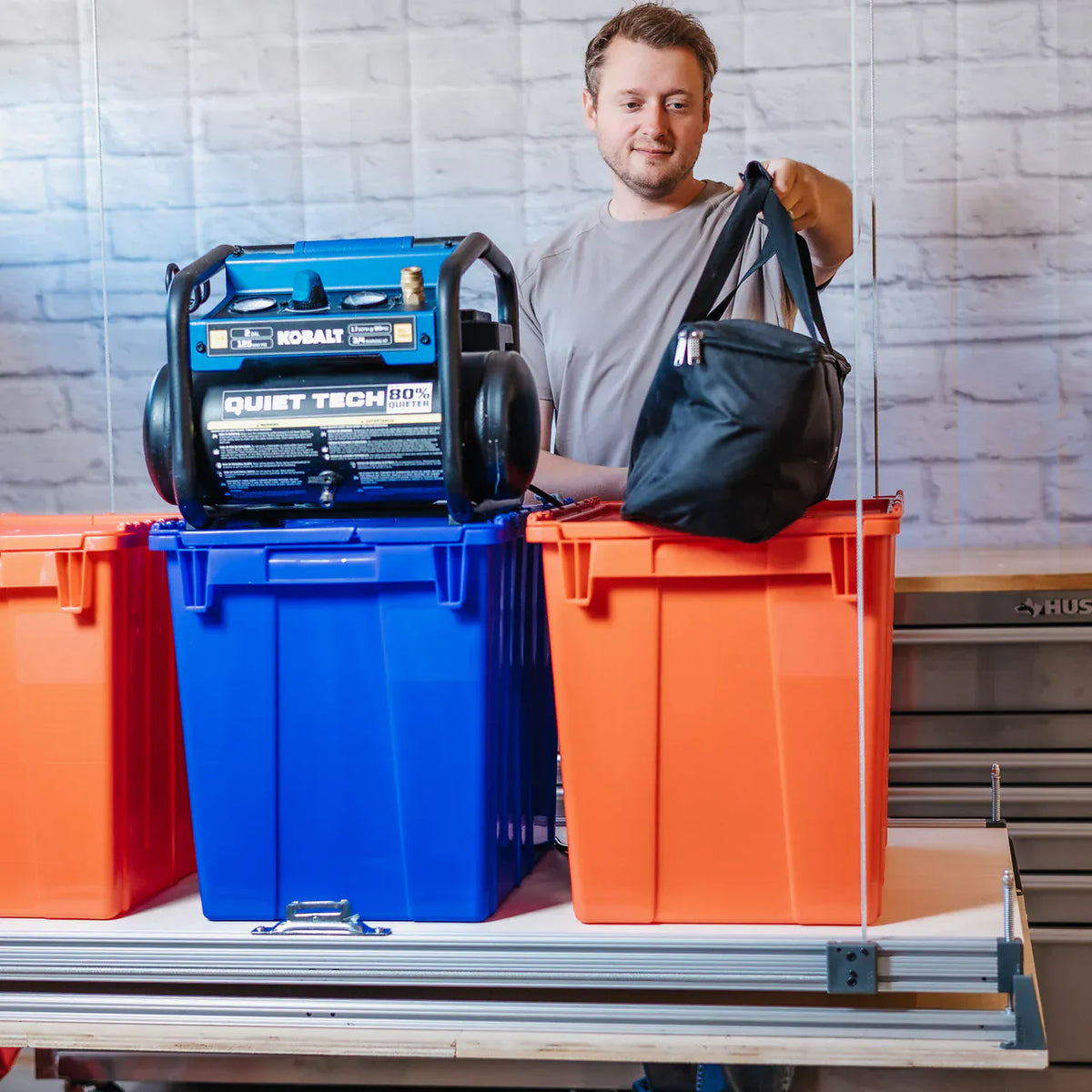 Man loading storage totes and a portable air compressor onto the lowered Attic-Lift platform
