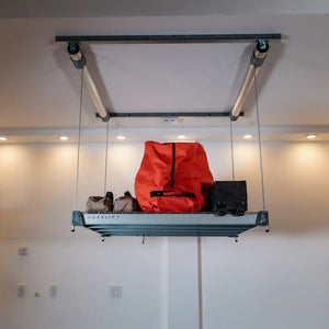 Auxx-Lift platform raised near the ceiling holding duffel and gear bags, AUXXLIFT logo on the side rail