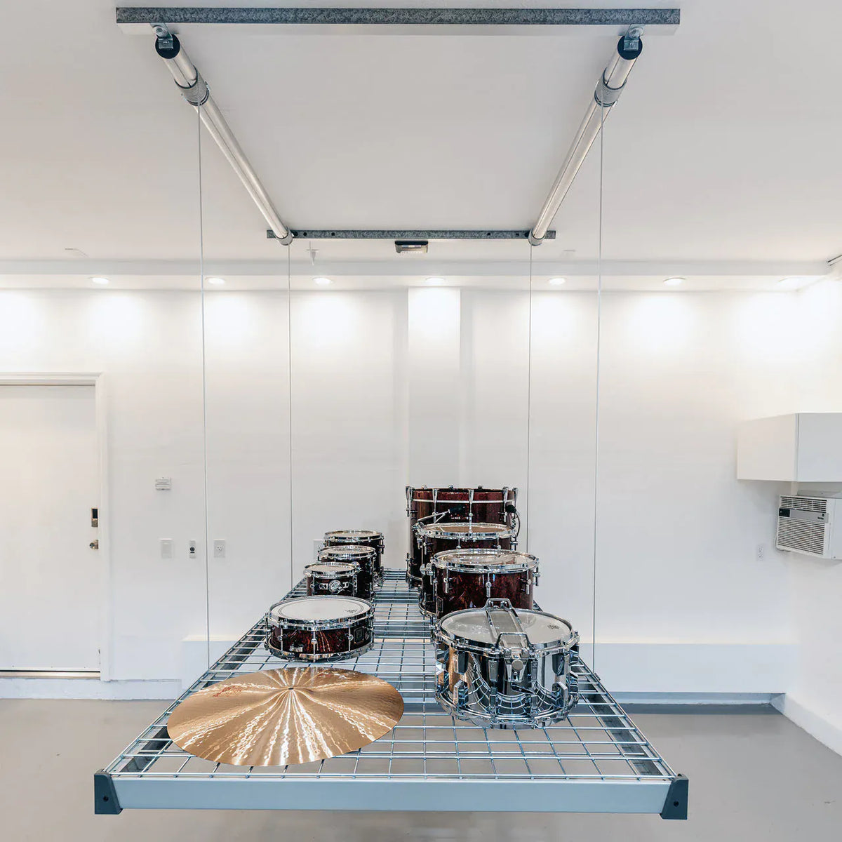 Auxx-Lift garage storage platform suspended from the ceiling holding a full drum kit in a white garage