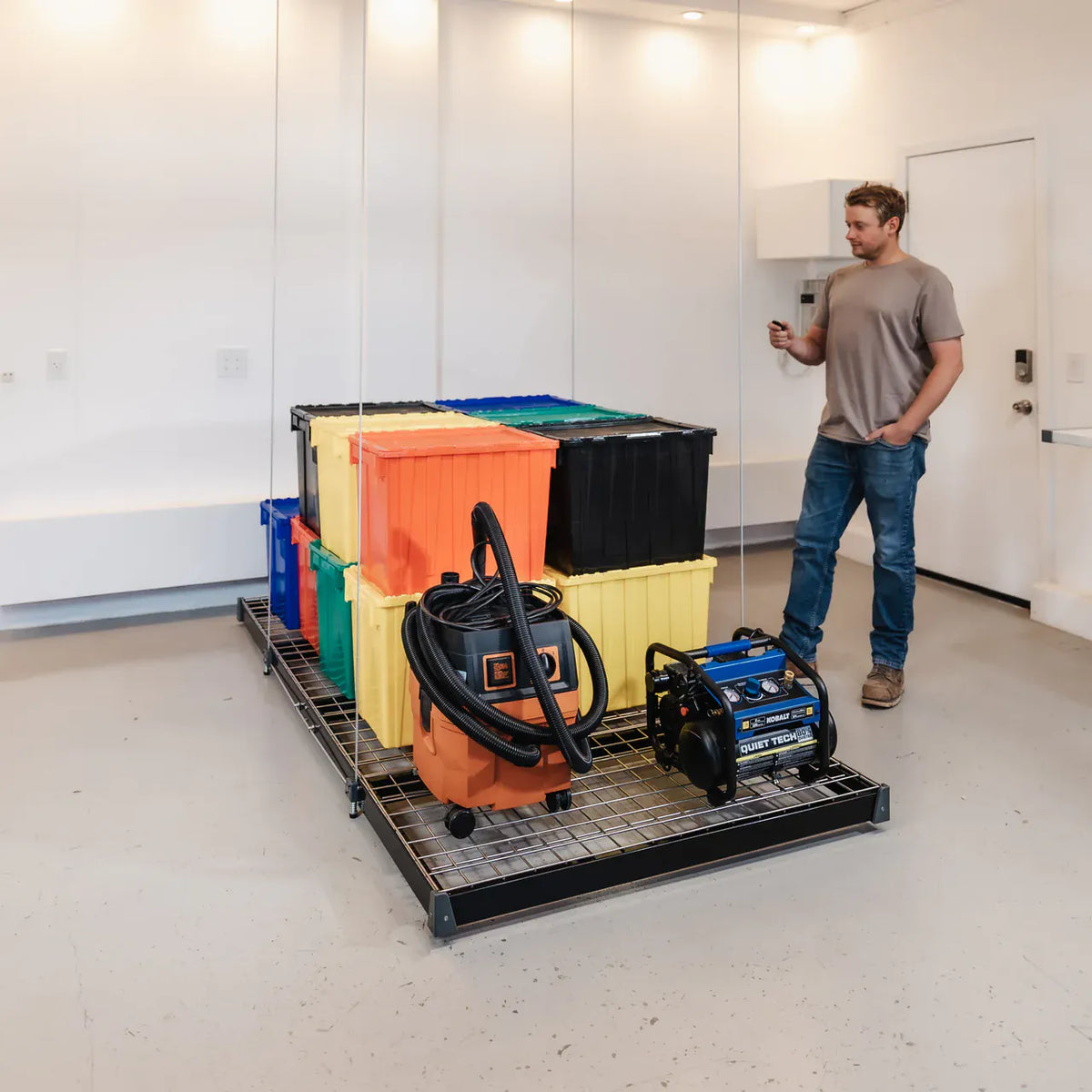 Man holding the remote beside a loaded Auxx-Lift platform at floor level in a garage