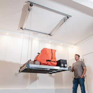 Man standing beside an Auxx-Lift platform raised near the ceiling with duffel bags and a case