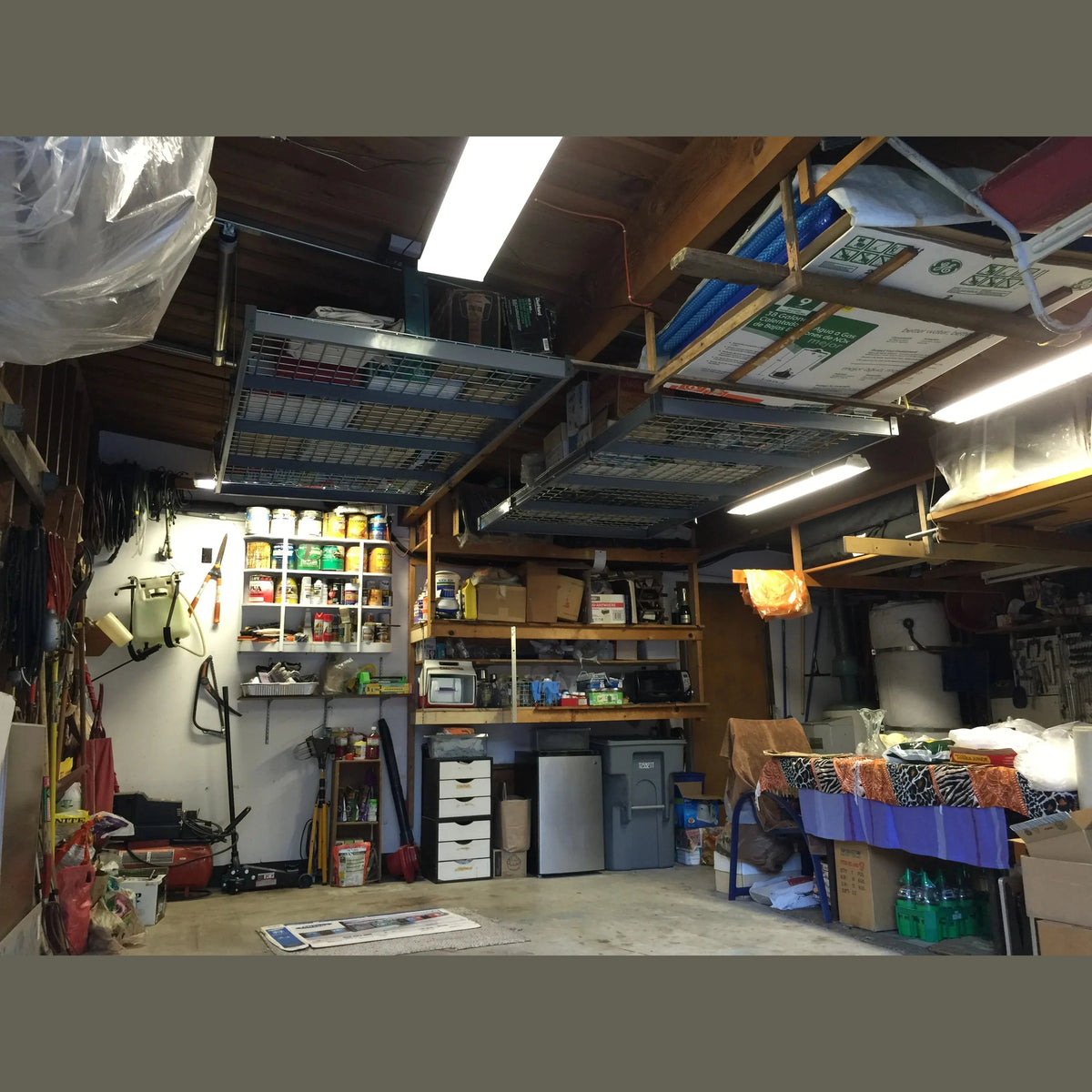Two Auxx-Lift wire-mesh platforms installed on a wood-joist workshop ceiling, loaded with gear