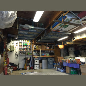 Two Auxx-Lift wire-mesh platforms installed on a wood-joist workshop ceiling, loaded with gear