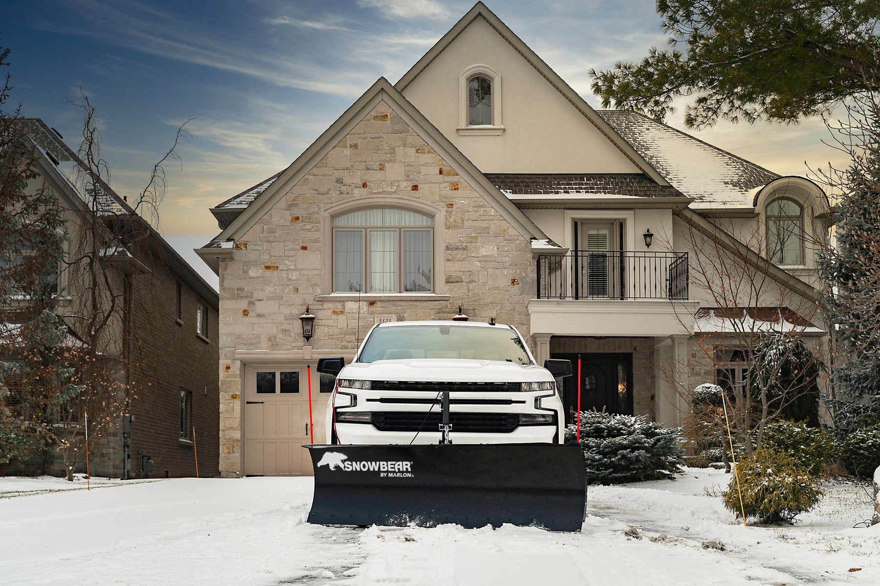White pickup with a SnowBear plow parked in a snowy driveway in front of a house