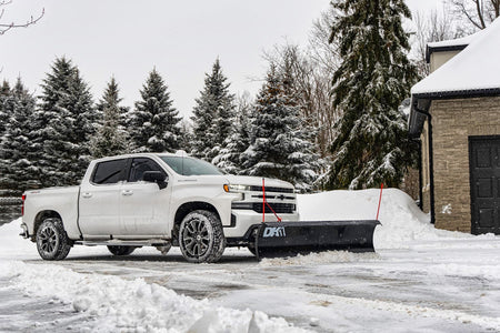White Chevrolet Silverado with the DK2 Everest plow angled while clearing a driveway