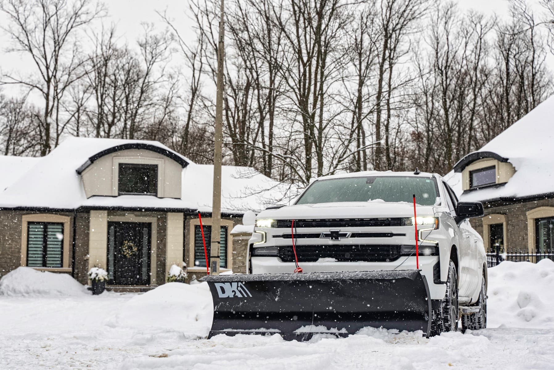 Front view of a white Chevrolet pickup with the DK2 Everest plow in falling snow