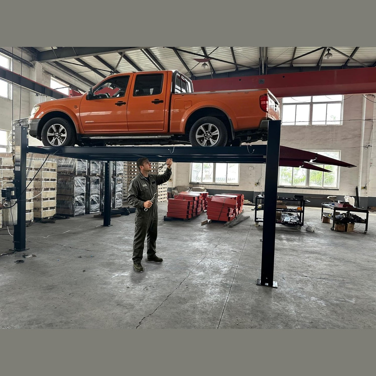 Technician working beneath an orange pickup raised on the four-post lift in a shop