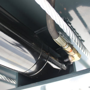 Black hydraulic cylinder end with hose fitting beside a steel lifting cable
